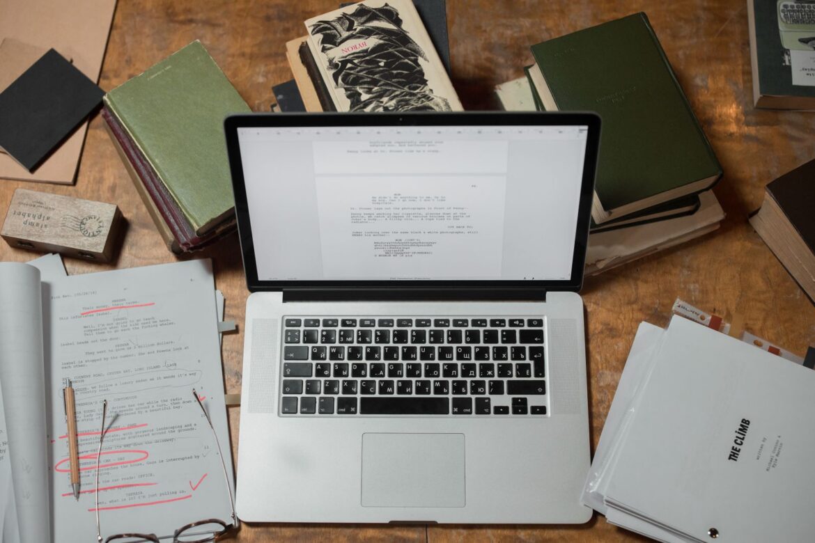 Laptop surrounded by books on wooden desk