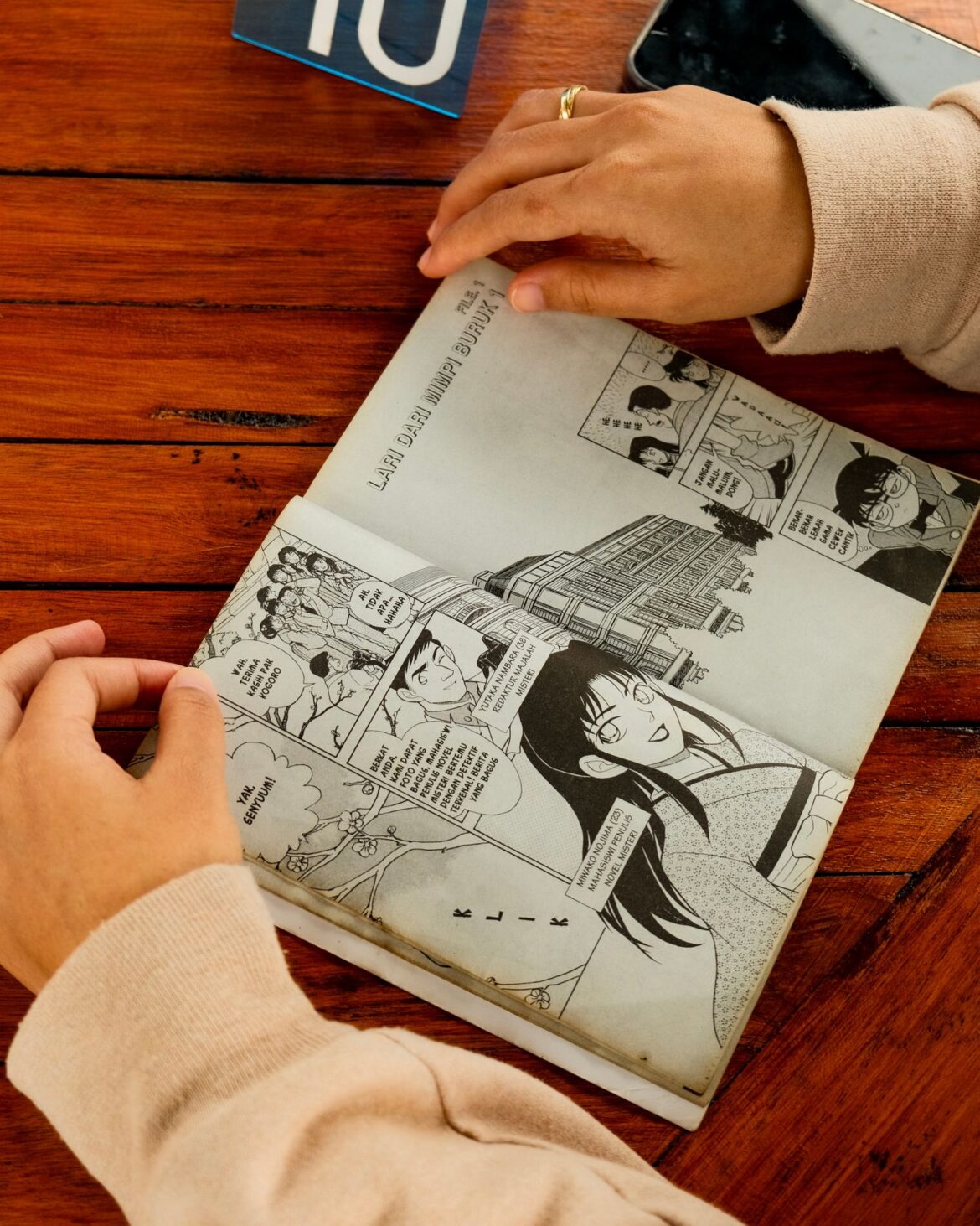 Hands holding manga book on wooden table