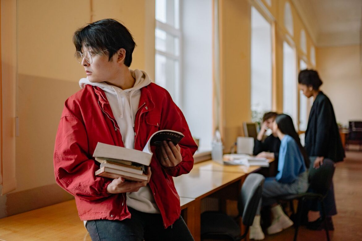 Young adult student holding books in library